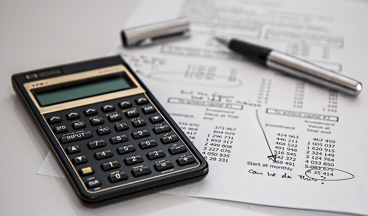 Calculatrice et stylo posés sur un tableau financier chiffré, illustrant la gestion de trésorerie d'une petite entreprise.