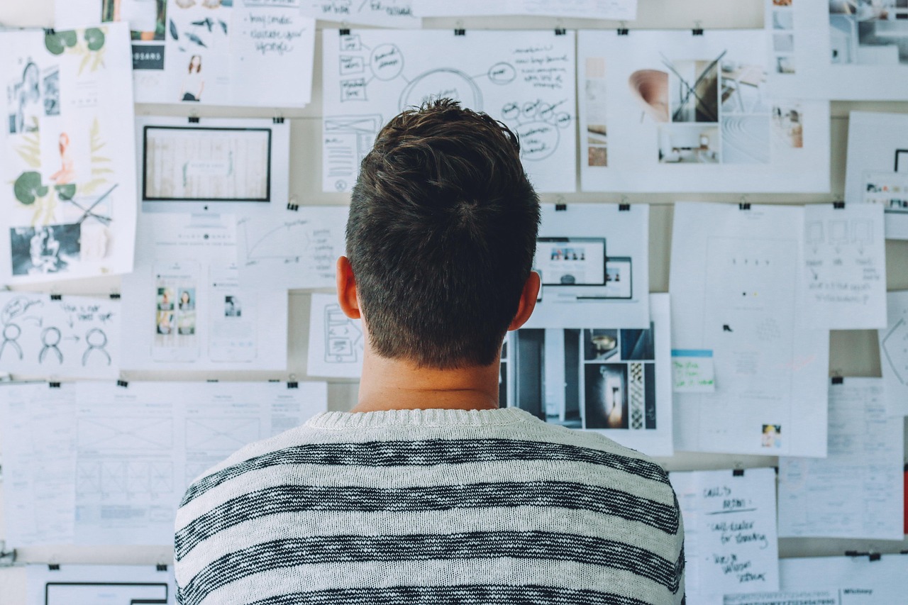 Entrepreneur de dos réfléchissant devant un mur couvert de plans, croquis et notes